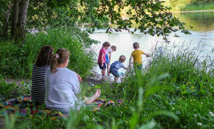 Parents sat on the riverbank watching children paddle and play in the river.